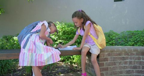 African American Girls Studying Together on Outdoor School Bench with Backpacks