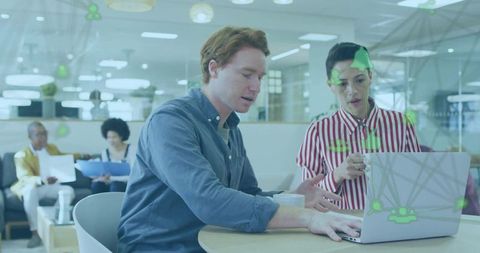 Young professionals collaborating on laptop with network overlay in modern office lounge