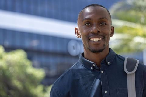 Smiling young professional standing outdoors with backpack on urban campus sunlit portrait