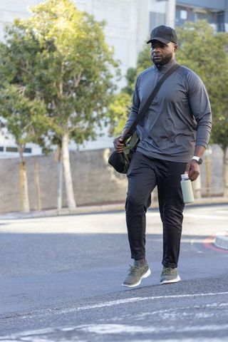 Active urban man walking with water bottle and crossbody bag in casual athletic wear
