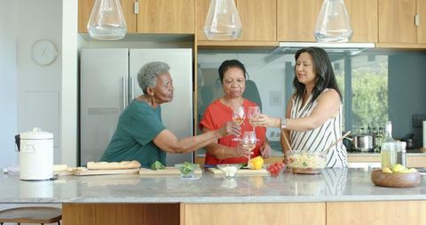Multigenerational diverse women toasting at kitchen island while serving salad and wine