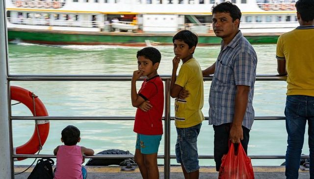 Father holding red bag watching ferry while children waiting at busy waterfront pier