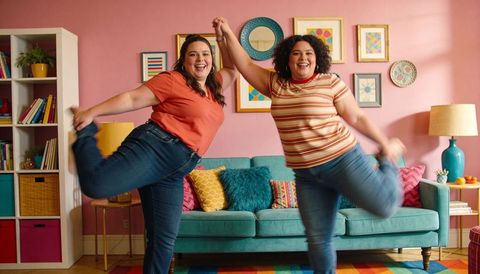 Plus-size friends dancing and balancing in colorful living room with teal sofa