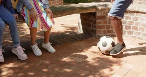 African teens sitting on bench controlling soccer ball in sunny brick courtyard