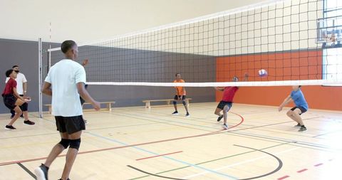 Diverse men's indoor volleyball team playing competitive match on bright hardwood court