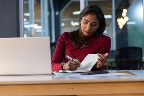 Focused Indian professional writing notes at laptop in modern coworking office for productivity