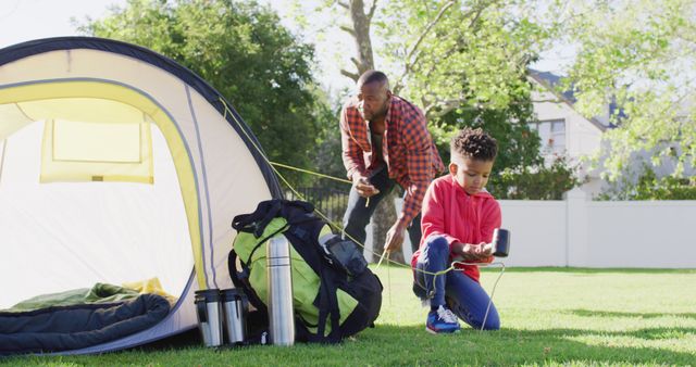 This image shows a father and son working together to pitch a tent in their backyard. Ideal for use in family-oriented content, outdoor activity promotions, or articles about family bonding and spending quality time outdoors.