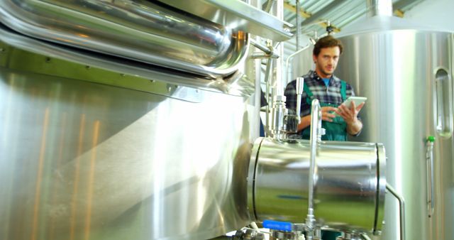 Engineer using digital tablet while inspecting brewery equipment. Can be used for topics on modern brewing technology, industrial processes, beer production, or professional occupations in the brewing industry.