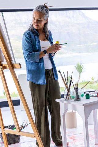 Senior woman painting at easel in coastal studio, creative retirement lifestyle scene