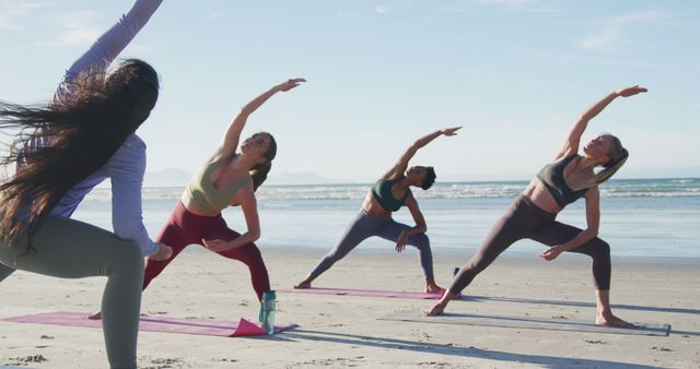 Young women practicing yoga on beach during sunset. Scene captures group doing yoga poses on mats with ocean view in background. Could be used for promoting wellness retreats, fitness classes, healthy lifestyle blogs, travel destinations focused on wellness.