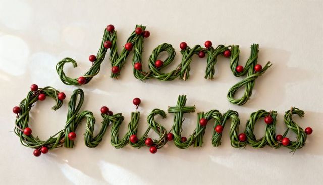Merry Christmas braided evergreen lettering with red berries flatlay on cream background