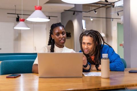 African american colleagues collaborating over laptop at modern coworking wooden table