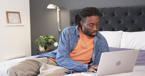 African American man working from bed on laptop, remote work productivity and home focus
