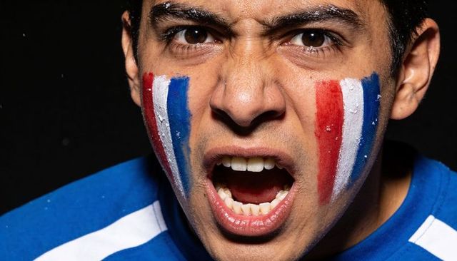 Intense sports fan shouting with red white blue face paint wearing blue team jersey