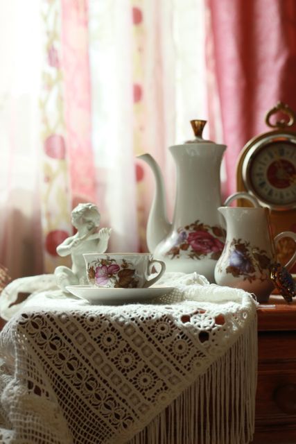 Vintage tea set with delicate lace tablecloth and various decorative elements ideal for promoting retro or vintage home decor. Perfect for illustrating concepts of elegant living, nostalgia, and cozy relaxation. Can be used in magazine articles about home decoration, blog posts on vintage interiors, and social media content for antique shops or tea brands.