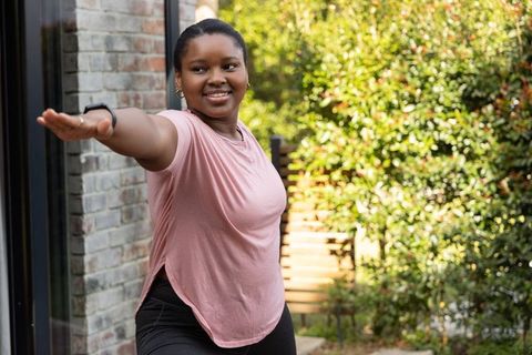 African american woman practicing yoga stretch on sunny patio in pink top and leggings