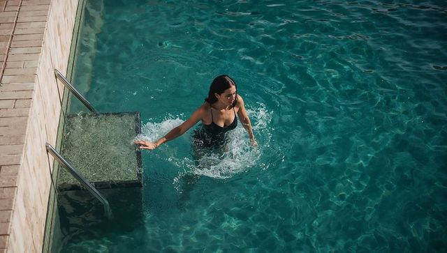 Sunlit woman wading in turquoise pool holding handrail on submerged steps, summer leisure
