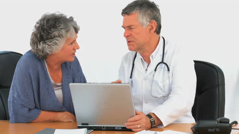 Doctor Discusses Medical Information with Senior Patient Using Laptop