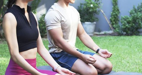 Asian couple practicing outdoor meditation on yoga mats in sunny backyard garden
