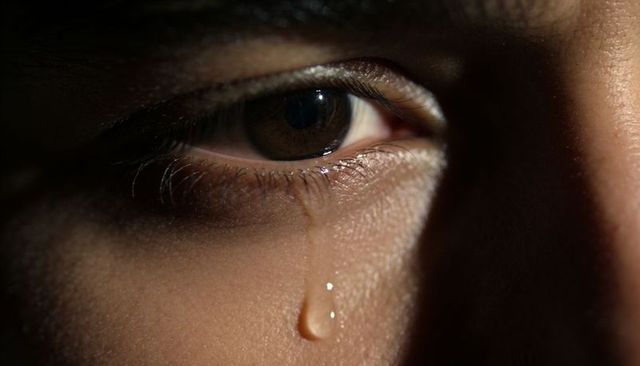 Close-up brown eye releasing single tear on cheek dramatic low-light emotional macro