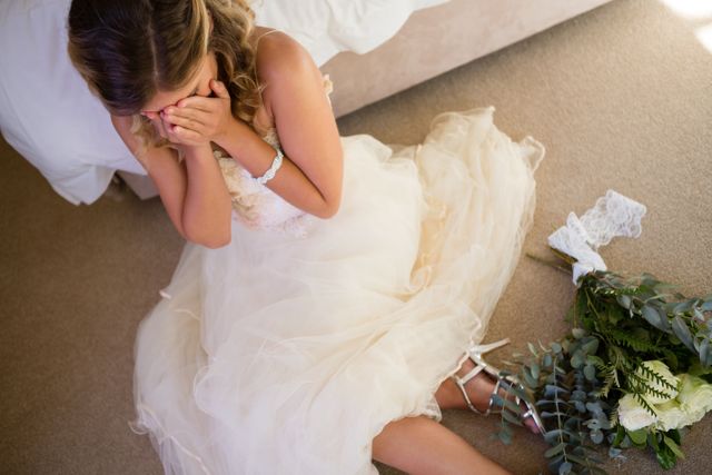 High angle view of bride in wedding dress crying while sitting by bed at home