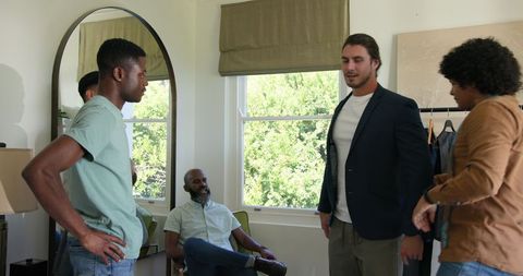Tailor measuring groom for wedding suit with friends watching