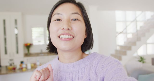 This image of a smiling woman taking a selfie in a modern home interior can be used for lifestyle blogs, social media posts, and advertisements. It reflects happiness, positivity, and contemporary living.