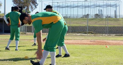 Baseball Players Stretching in Green and Yellow Uniforms During Outdoor Team Practice