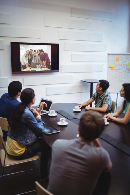 Business professionals engaging in a video conference in a modern conference room. Ideal for themes on remote work, corporate meetings, communication, and teamwork. Useful for illustrating modern workplace dynamics, technology in business, and collaborative efforts.