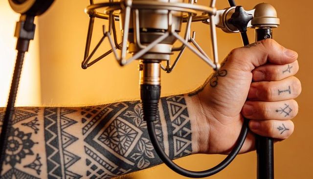 Holding tattooed arm gripping condenser microphone stand with visible xlr cable in amber studio