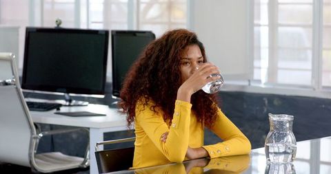 Woman in Yellow Sweater Drinking Water in Office Setting