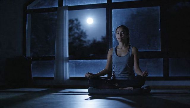 Woman meditating under full moon on zafu with yoga mat nighttime mindfulness and calm