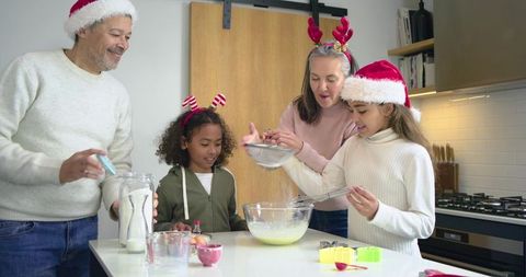 Multicultural family mixing cookie batter at kitchen island wearing Santa hats for holiday baking