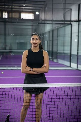 Indian woman standing confidently on purple indoor glass tennis court wearing black skort