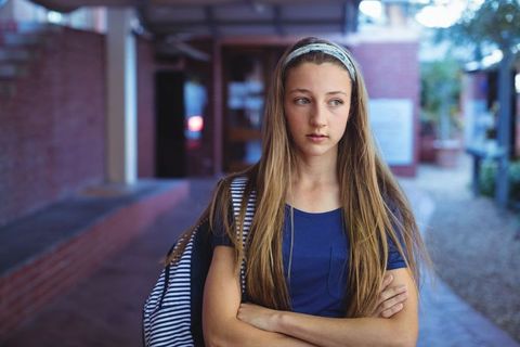 Thoughtful teenage girl at school entrance with backpack