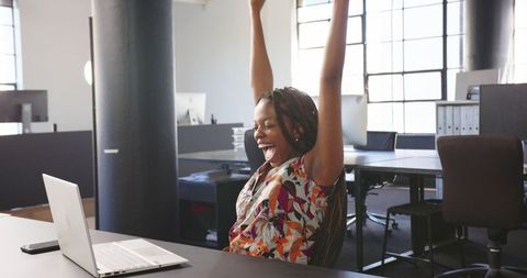 Woman celebrating achievement in modern office with laptop
