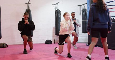 Teen fitness instructor leading group lunge workout in boxing gym coaching strength