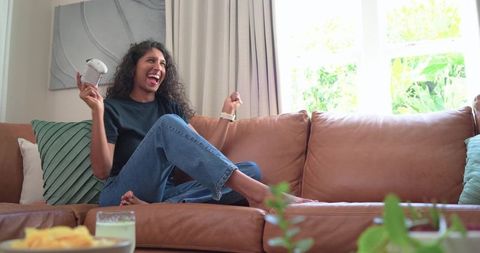 Laughing african american woman cheering and holding game controller on leather sofa
