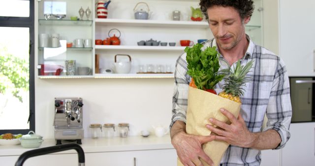 Focus is man bringing groceries into modern kitchen. Use for themes related to healthy eating, home cooking, or sustainability. Great for blogs or advertising organic products, kitchen appliances, or lifestyle content.
