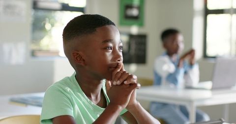 Thoughtful african american boy focusing on laptop in bright elementary classroom