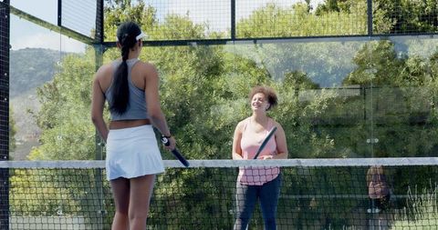 Female friends laughing and starting padel practice rally on sunny outdoor court