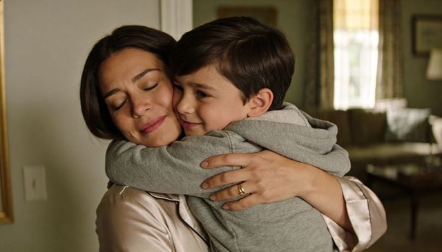Mother and son sharing warm hug with visible wedding ring and satin robe in cozy home