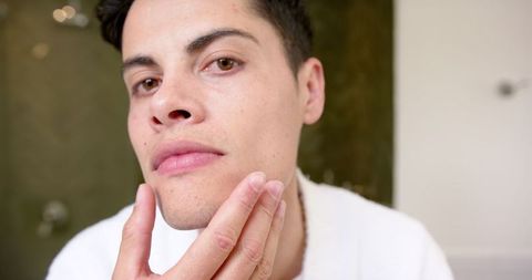 Man examining skin reflecting self-care routine in bathroom