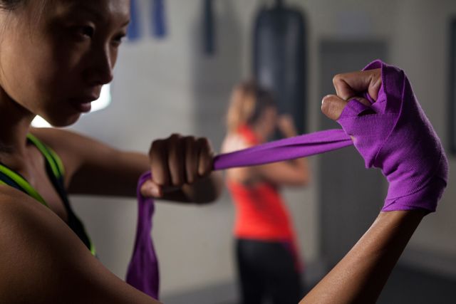 Woman wrapping hands with purple hand wrap in fitness studio. Ideal for use in articles or advertisements related to fitness, boxing, training routines, gym equipment, or athletic preparation.