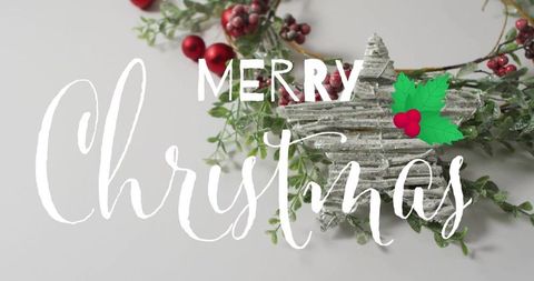 Merry christmas script over rustic star wreath featuring red berries on gray tabletop