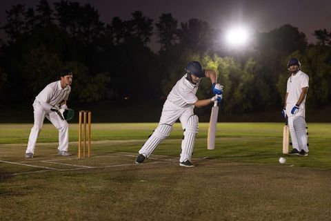 Night cricket under floodlights with batsman executing forward drive and fielders