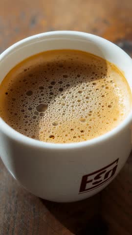 Vertical Closeup of Espresso Cup Releasing Crema and Frothing Surface on Rustic Counter