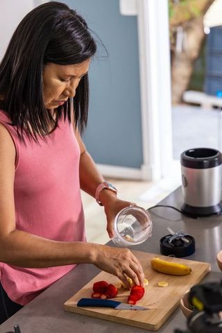 Asian woman preparing banana and strawberry smoothie in bright minimalist home kitchen