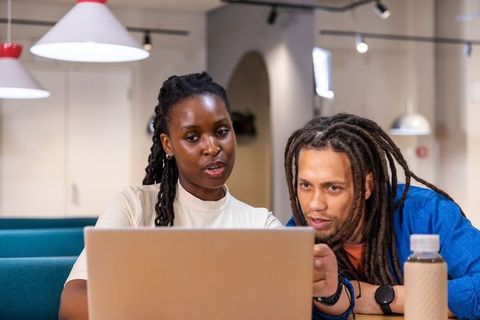 Black woman collaborating with coworker on laptop in coworking cafe boosting productivity