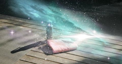 Sunlit folded pink towel and pump bottle on wooden deck with cosmic sparkle and lens flare